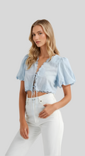Load image into Gallery viewer, Light blue puff sleeve crop top with lace-up front and scalloped hem, styled with high-waisted white jeans.
