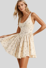 Load image into Gallery viewer, Woman wearing a cream floral mini dress with sleeveless scoop neckline and flared skirt – summer fashion outfit
