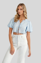 Load image into Gallery viewer, Light blue puff sleeve crop top with lace-up front and scalloped hem, styled with high-waisted white jeans.
