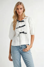Load image into Gallery viewer, White puff sleeve blouse with black bow tie accents, made from 100% rayon, styled with light blue jeans.
