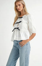 Load image into Gallery viewer, White puff sleeve blouse with black bow tie accents, made from 100% rayon, styled with light blue jeans.
