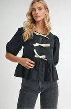 Load image into Gallery viewer, Black puff sleeve blouse with black bow tie accents, made from 100% rayon, styled with light blue jeans.
