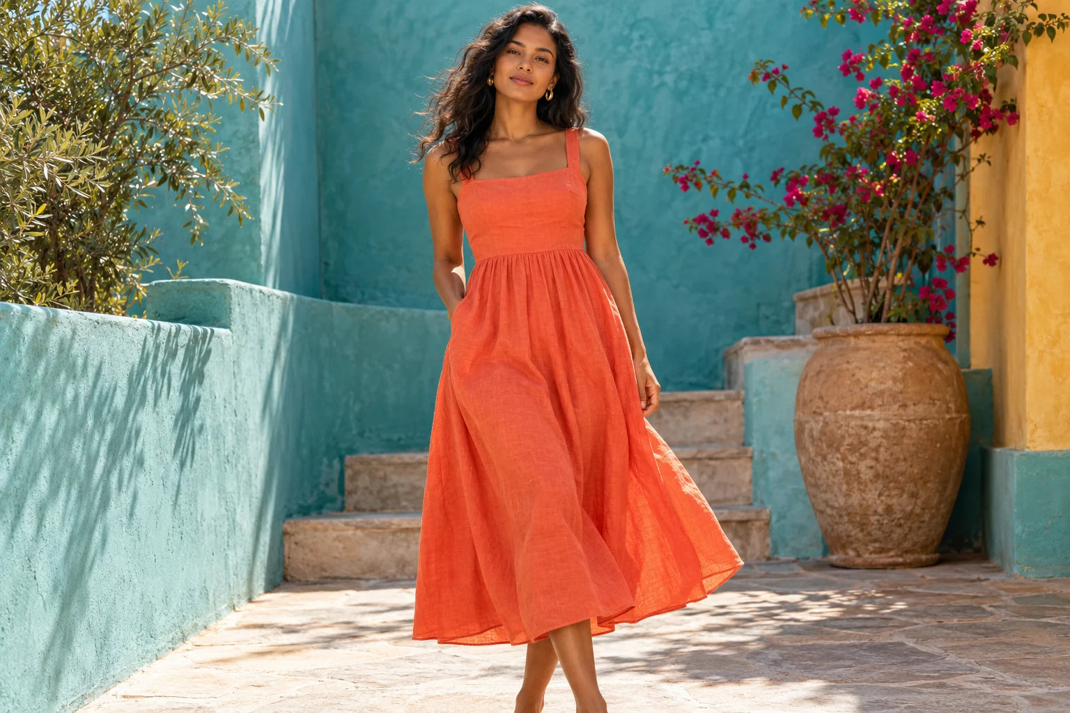 Woman in a vibrant coral midi dress against sunlit turquoise walls